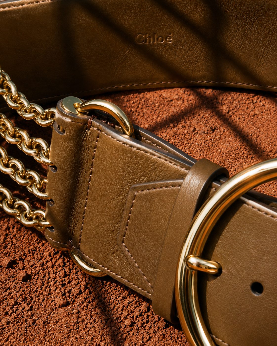 Gold chain and leather belt detail on red clay