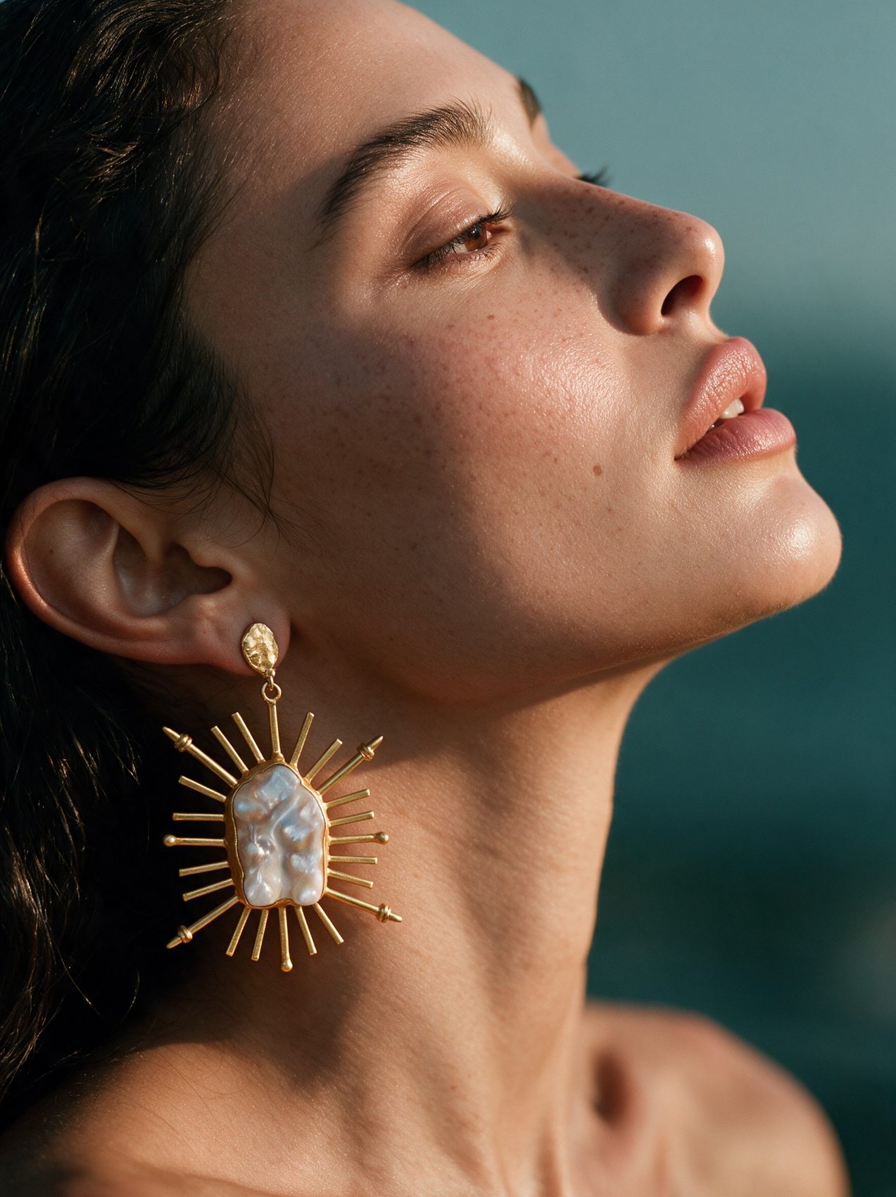 Profile of model with a gold sunburst pearl earring against the sea