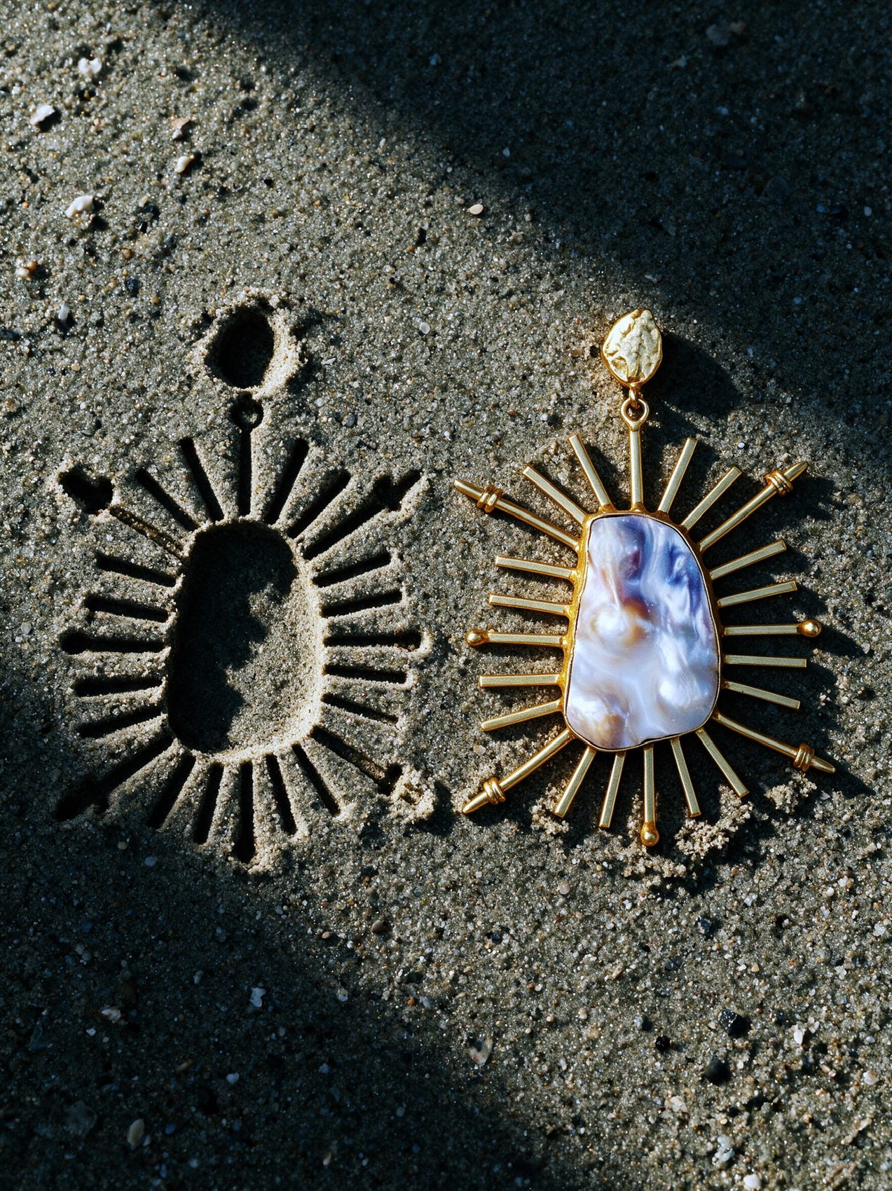 Sunburst earring beside its own imprint in sand