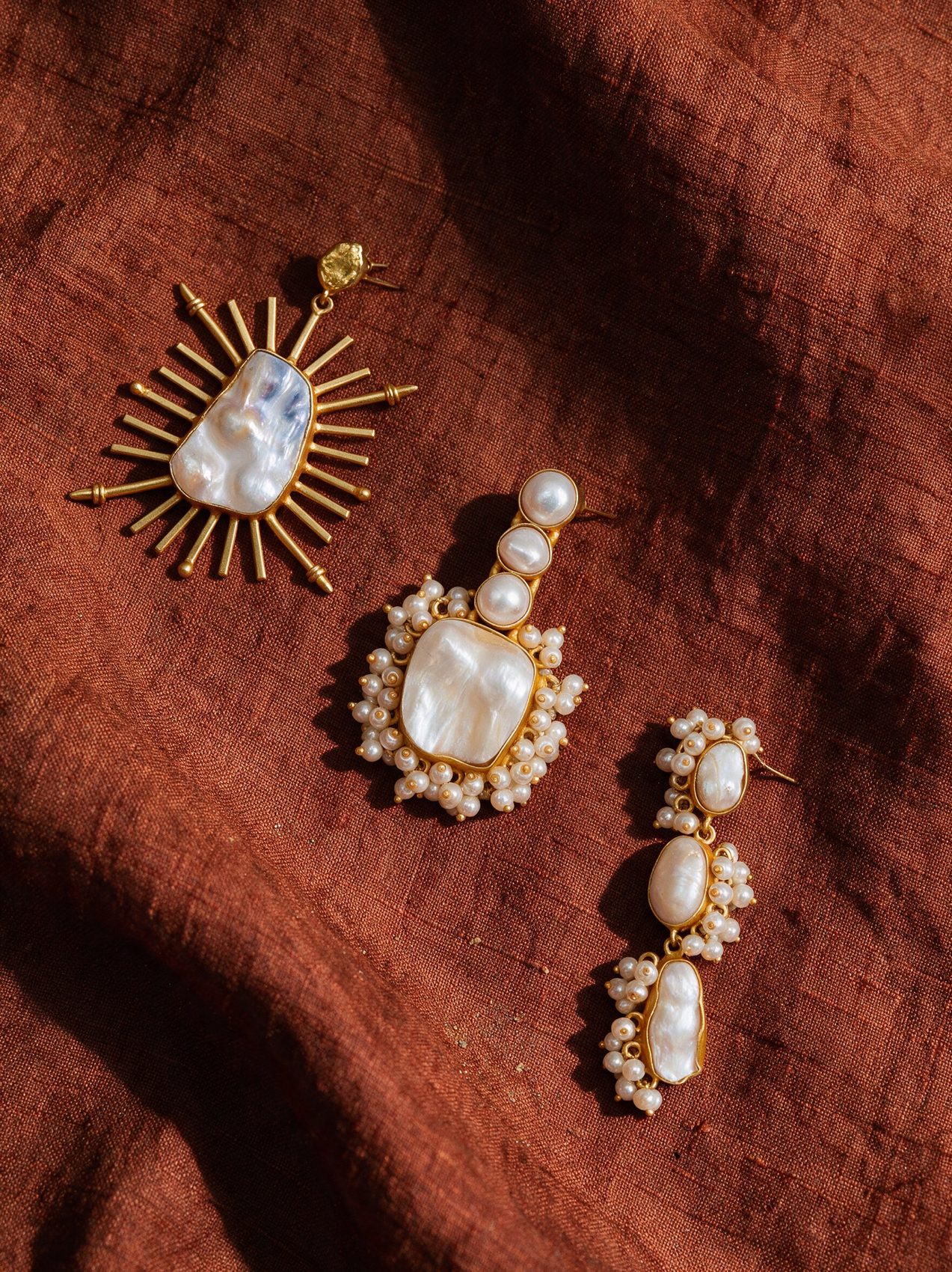 Two sunburst earrings spilling from a conch shell on linen
