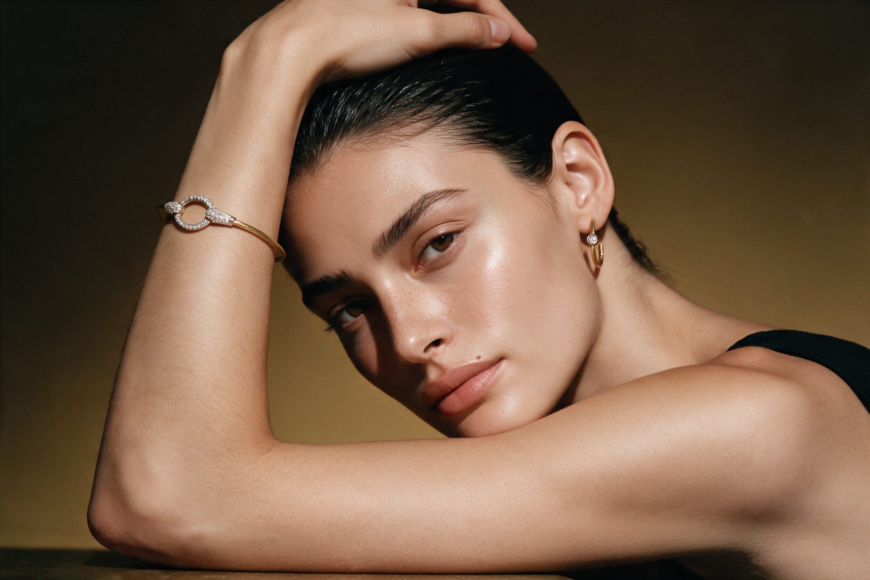 Model resting her head on her arm, wearing a pavé cable cuff and hoop