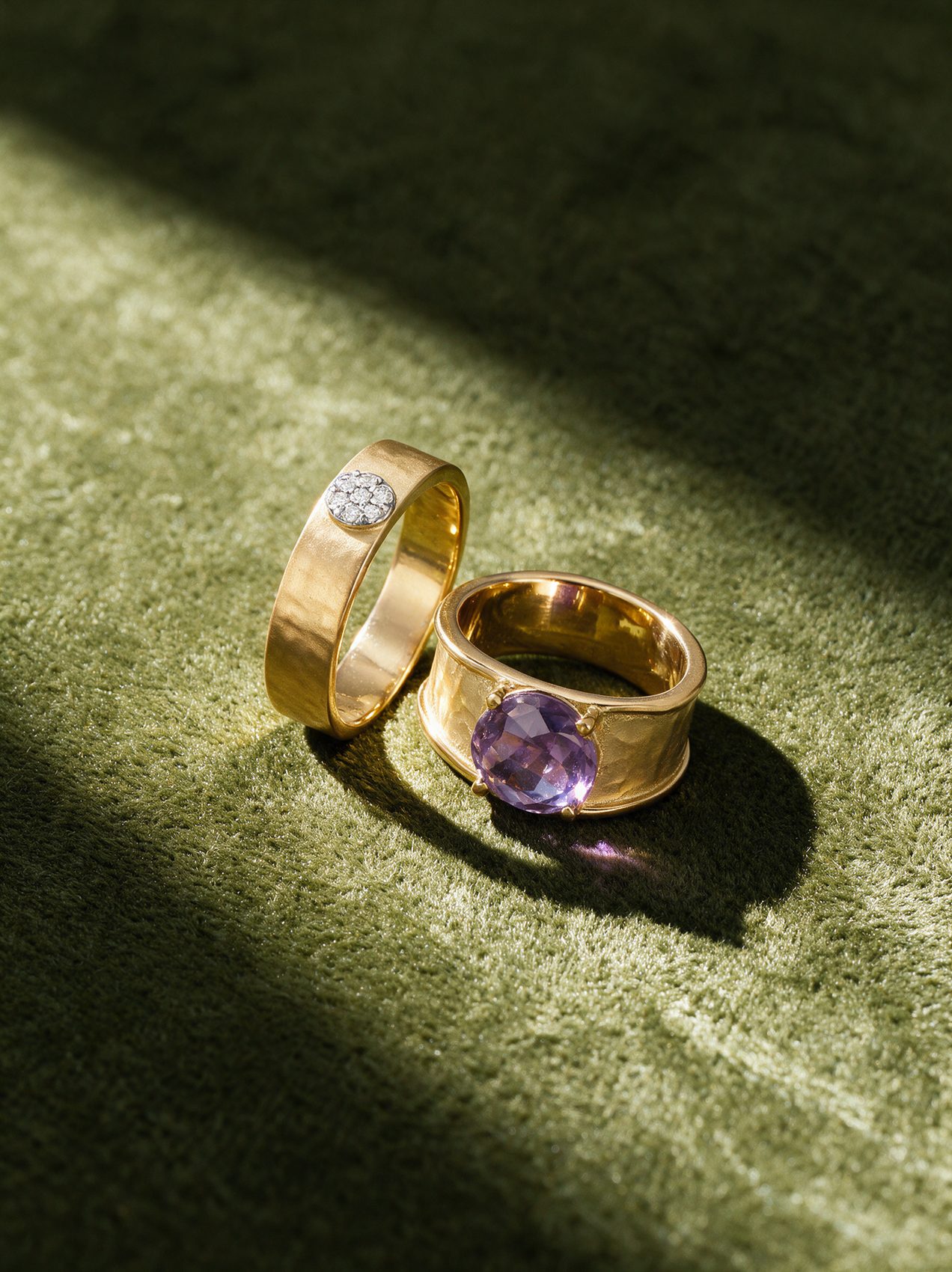 Two gold rings, one pavé and one amethyst, on olive velvet